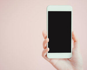 Hand holding a white smart phone in front of a pink background