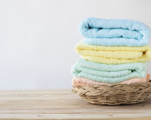 A stack of folded towels in a brown basket in front of white background