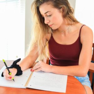 Girl sitting at an orange table holding a pen writing into a journal