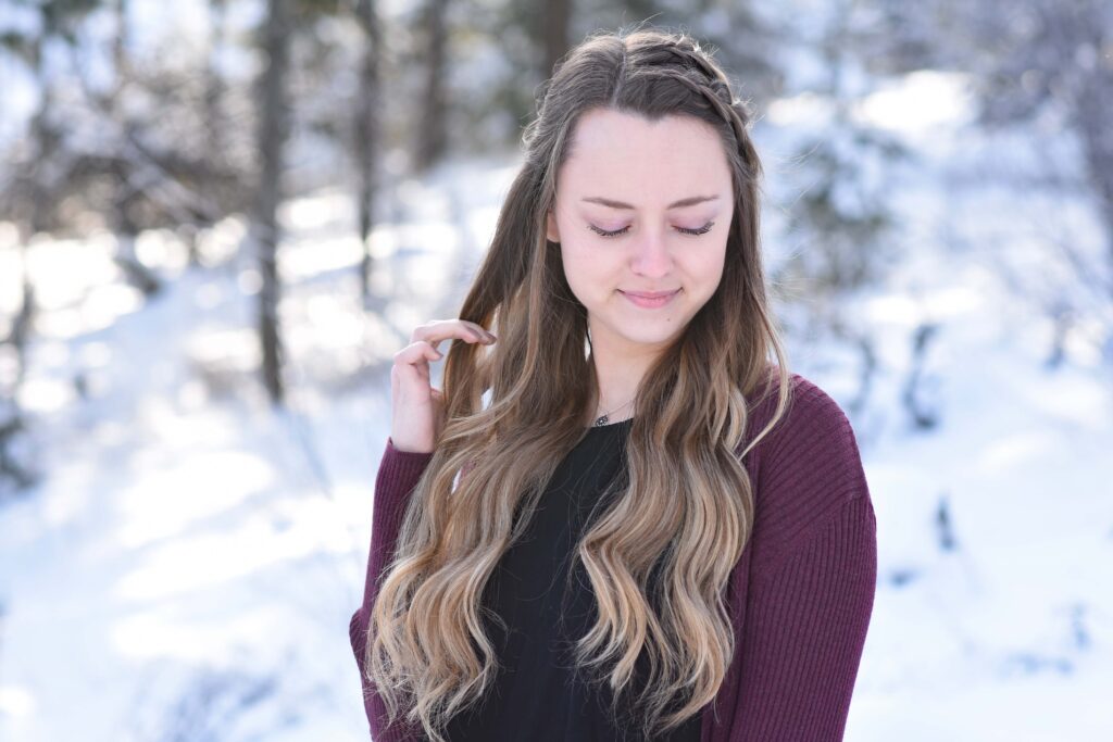 Portrait of girl looking down while standing outside in a snowy forest modeling the "Double Dutch Half-Up" hairstyle