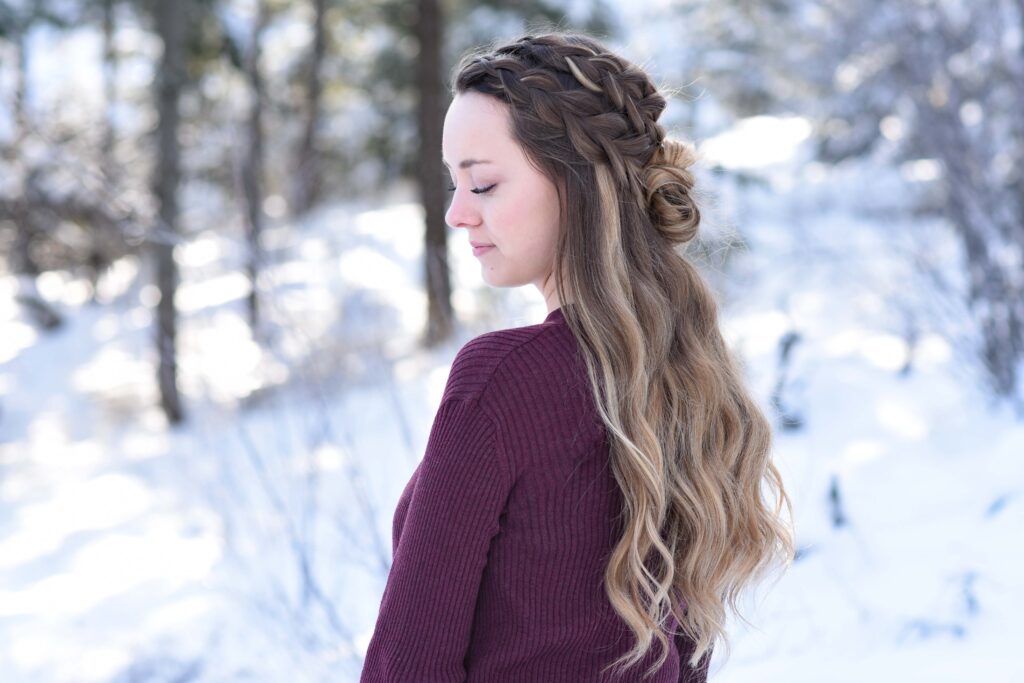 Profile of girl looking down while standing outside in a snowy forest modeling the "Double Dutch Half-Up" hairstyle
