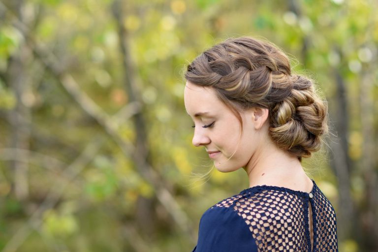 Side profile of smiling girl looking downwards standing outside modeling the "French Braid Updo" hairstyle