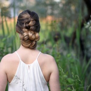 Back view of girl with a white dress standing outside in greenery and modeling "Knotted Braid Updo" hairstyle.