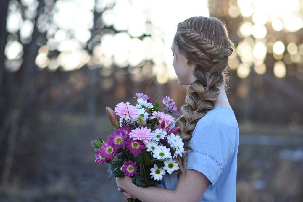 Profile view of a young girls holding flower bouquet modeling "Side Pull-Thru Combo" hairstyle