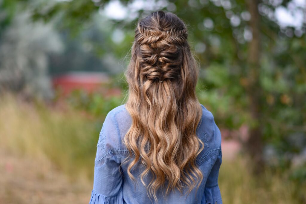 Back view of young girl wearing a blue shirt standing outside modeling "Twisted Fishtail" hairstyle 