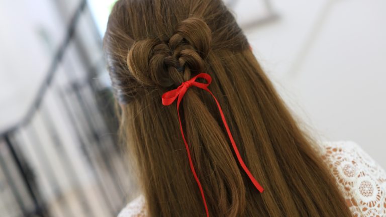 Back view of girl standing indoors wearing a red ribbon in her hair modeling the "Butterfly Tieback" hairstyle.
