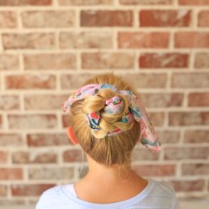 Back view of girl with a white shirt in front of brick background modeling "Braided Scarf Bun" hairstyle