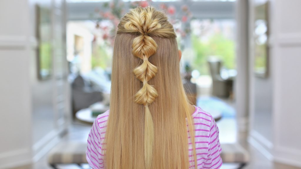 Back view of a young blonde girl standing indoors modeling the "Triple Flip Flips" hairstyle