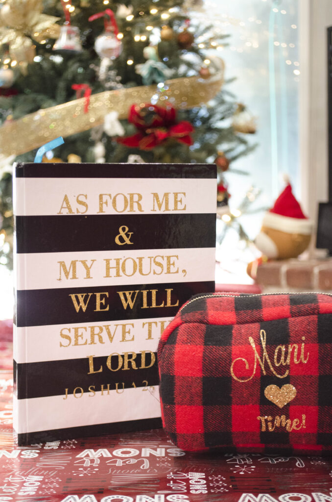 A black and white journal next to a red plaid makeup back placed close to a Christmas tree