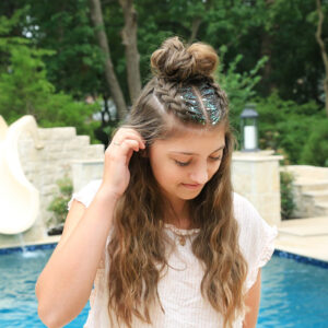 Girl standing by the pool with glitter in her hair modeling Double Dutchbacks into a Messy Bun hairstyle