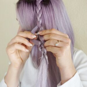 Woman wearing a white shirt braiding her lavender dyed hair