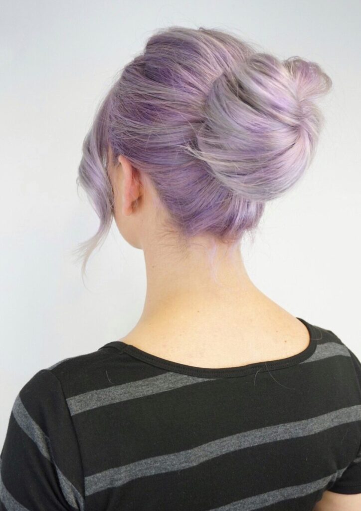 Back view of girl with lavender modeling her hair in a "bun" in front of a white background