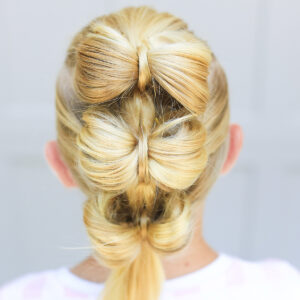 Back view of blonde girl standing outside in front of a white background modeling "Triple Bow Hawk" hairstyle