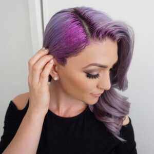 Side view of a young woman wearing a black shirt touching her purple hair and purple glitter gel
