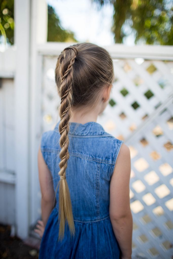 Back view of little girl wearing a denim dress standing outside modeling "Twist Wrap Ponytail"