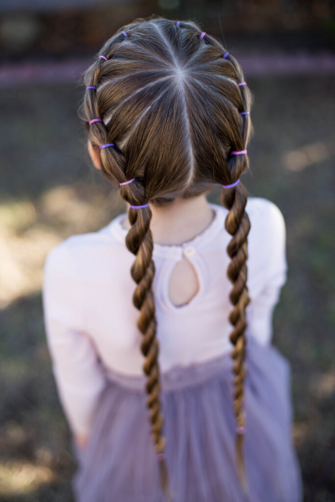 Back view of little girl standing outside in her tutu modeling "Banded Twist Braid" hairstyle