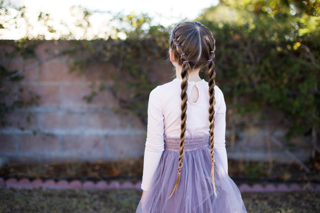 Back view of little girl standing outside in her tutu modeling "Banded Twist Braid" hairstyle