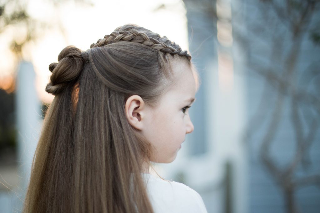Side profile of little girl with long hair standing outside modeling "Braided Bun Combo" hairstyle