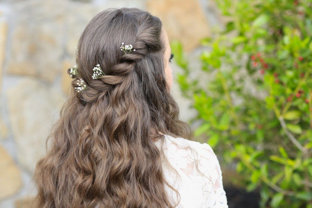 Back view of girl with flowers in her hair standing outside modeling the "Aurora Twistback" hairstyle