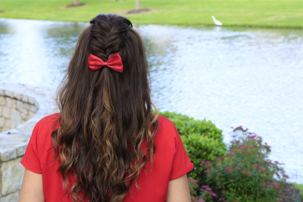 Back view woman wearing a red shirt and red bow in her hair standing by the lake modeling "Woven Faux Hawk" hairstyle