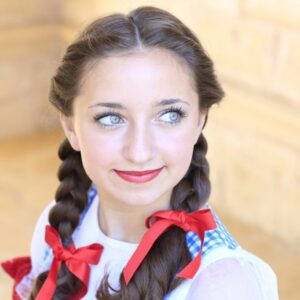 Portrait image of girl wearing costume with red ribbon in her hair modeling "Dorothy Braids" hairstyle