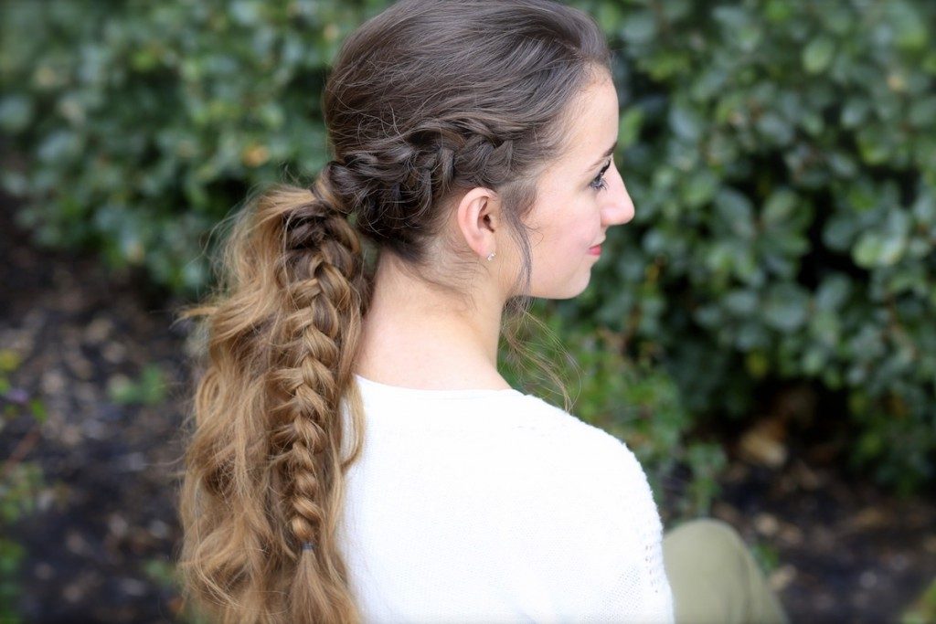 Side profile image of smiling girl standing in front of outside bushes modeling a "Viking Braid"