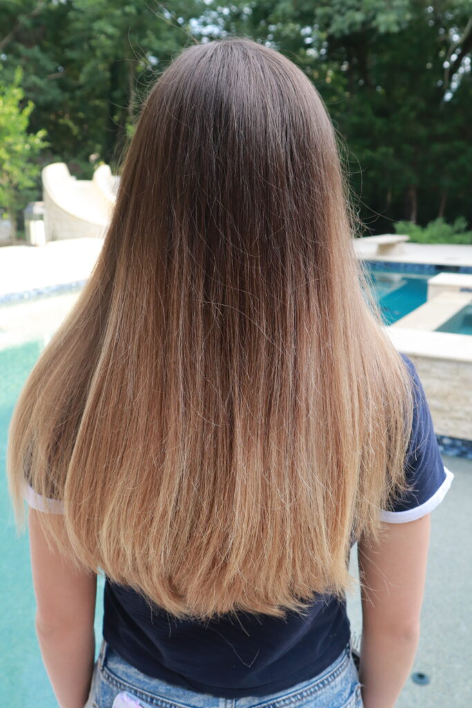 Back side of girl with long straight hair standing outside in front of the pool 