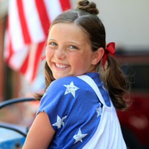 Side view of smiling girl during 4th Of July celebration modeling "Star Bun Combo" hairstyle
