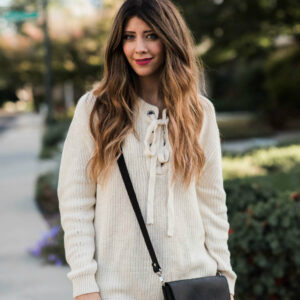 Woman outside wearing a white sweater, denim pants, and black crossbody bag