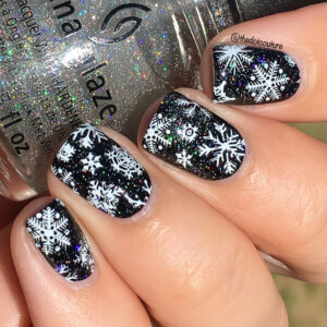 Black painted nails with white snow flakes holding a bottle of glitter nail polish