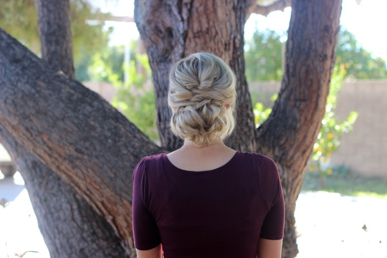 Back view of girl with a purple shirt standing outside modeling "Topsy Tail Bun" hairstyle. 