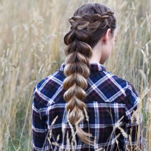Back view of young girl in the meadow wearing blue plaid shirt modeling "Wrapped Pull-Thru Braid" hairstyle